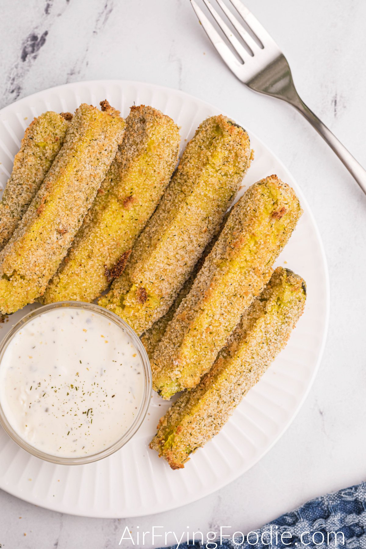 Crispy golden brown air fryer dill pickle spears on a white plate with dipping sauce.