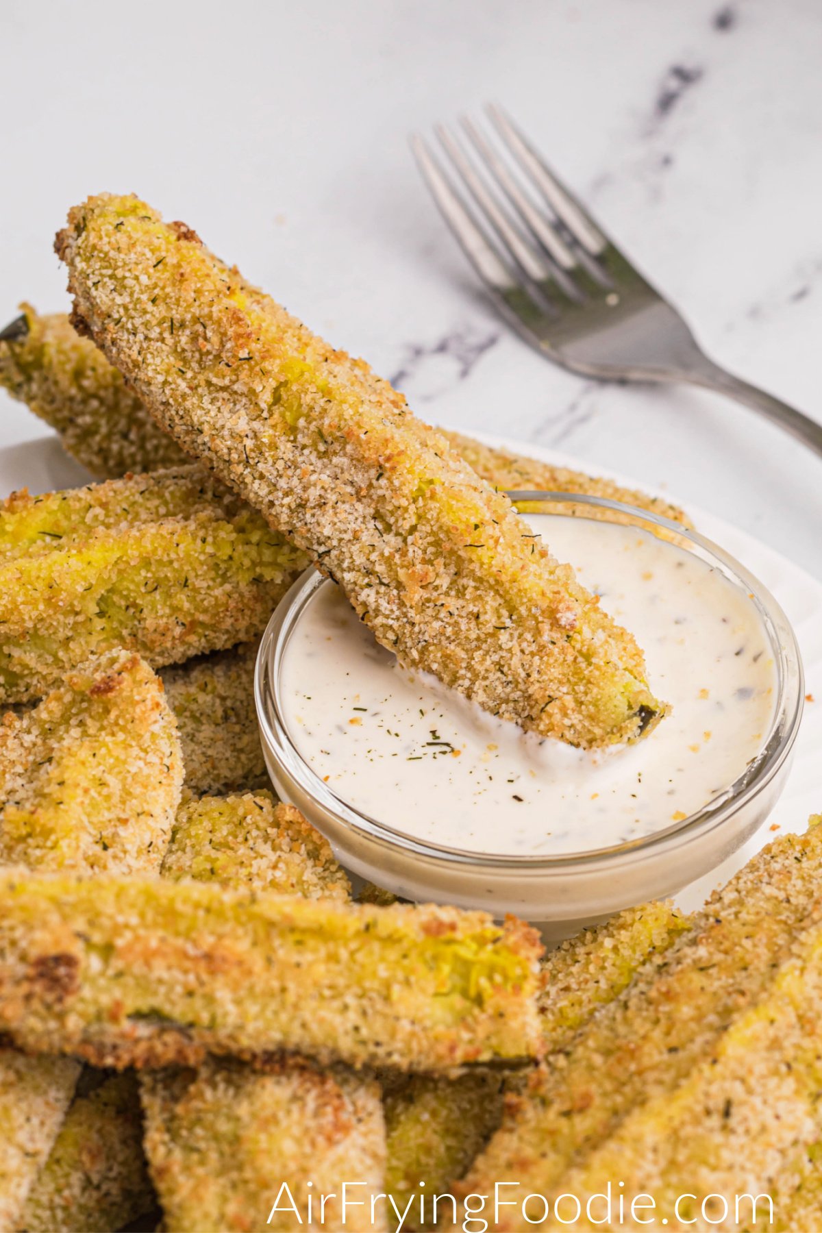 Crispy dill pickle spears on a white plate with dipping sauce. 
