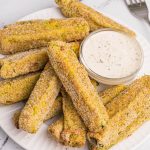 Overhead photo of crispy air fried dill pickles on a white plate with dipping sauce.