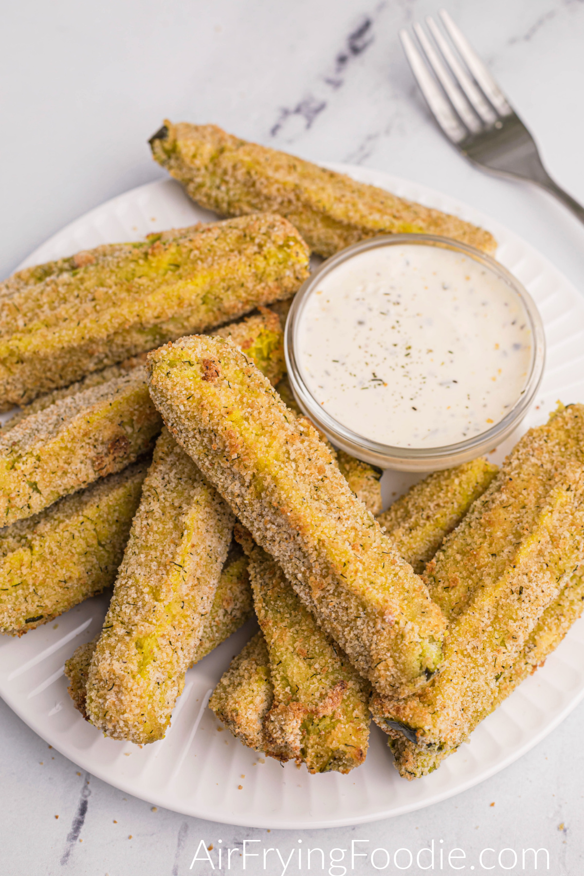 Crispy Air Fryer Dill Pickles cooked and ready to eat, served on a white plate with dipping sauce. 
