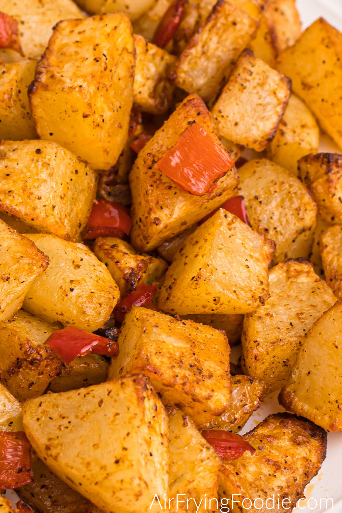 Air fried, cubed, and cooked russet potatoes with onion and bell pepper on a white plate, ready to serve. 
