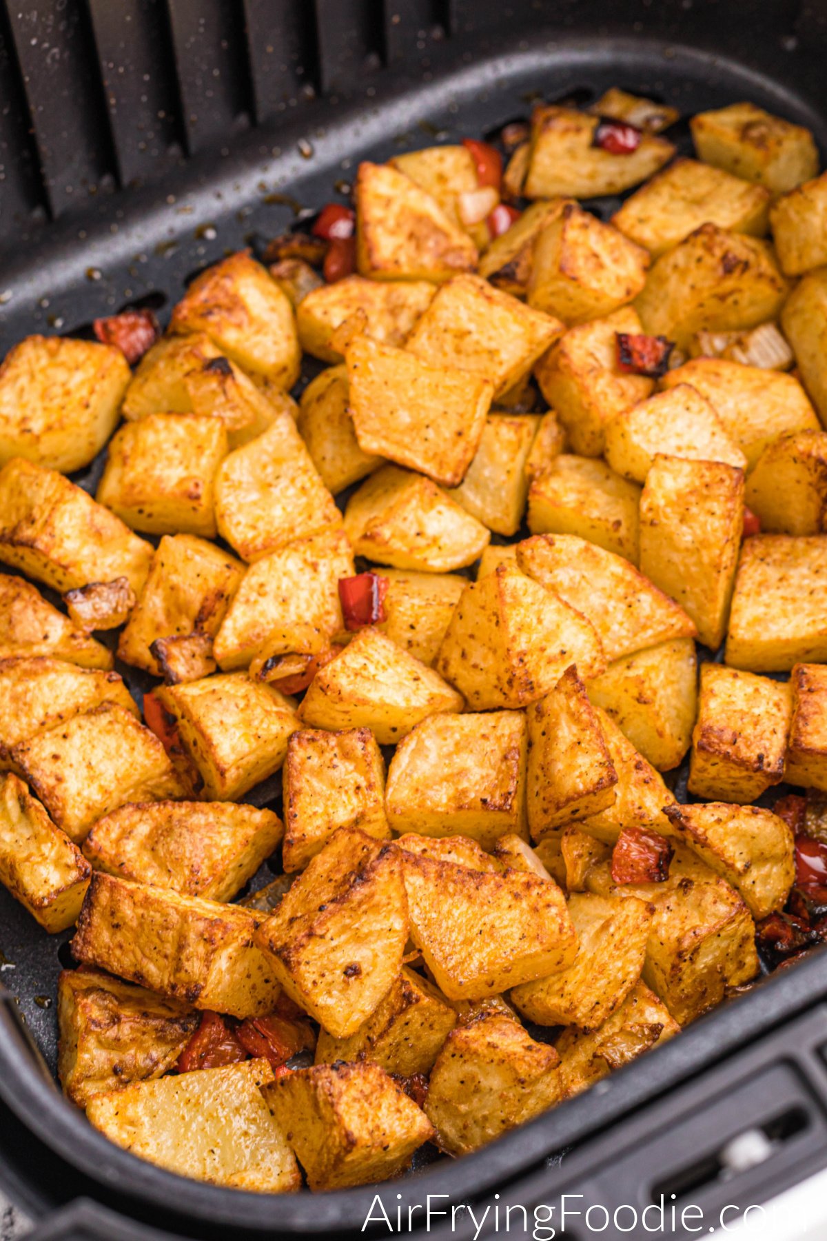 Home fries in air fryer basket, fully cooked and golden brown. 
