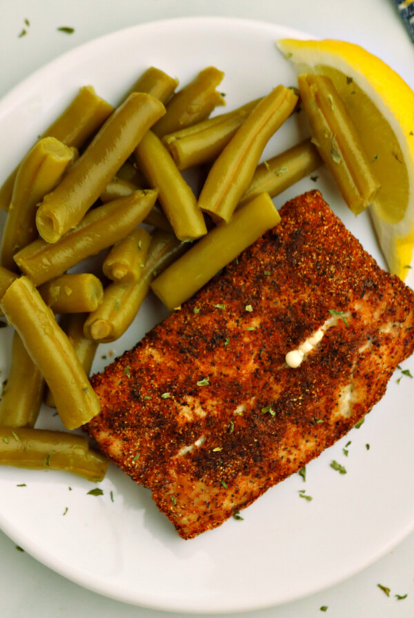 Overhead photo of air fried Mahi Mahi on a white plate with green beans and a lemon slice.