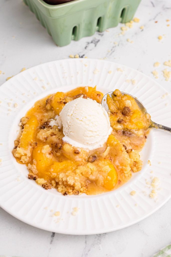 White plate with peach cobbler scooped out and topped with vanilla ice cream