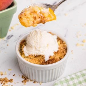 golden peach cobbler in a white ramekin with a spoonful lifted