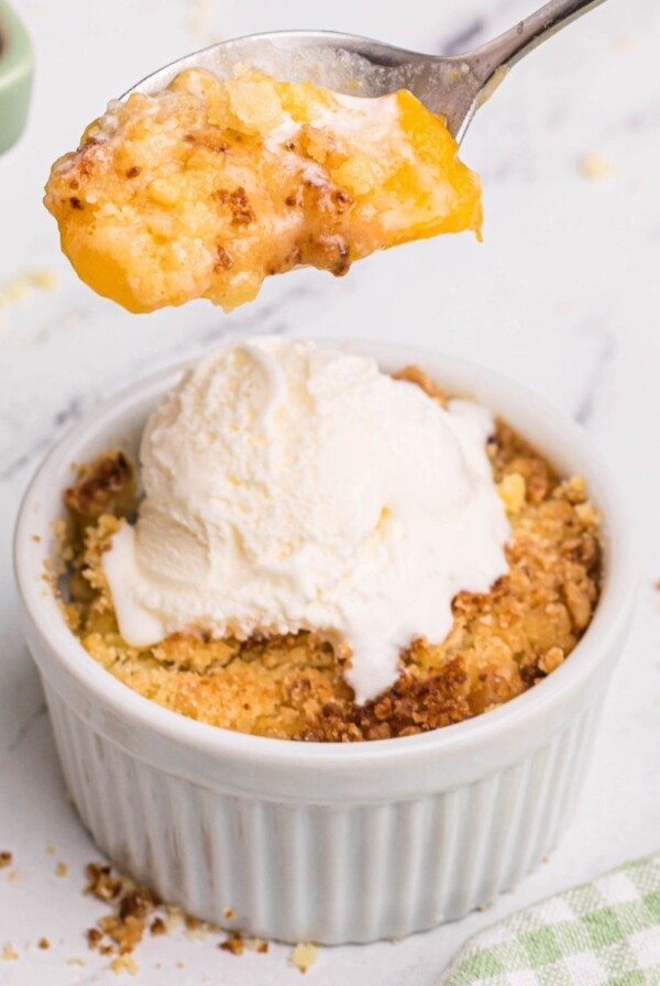 golden peach cobbler in a white ramekin with a spoonful lifted