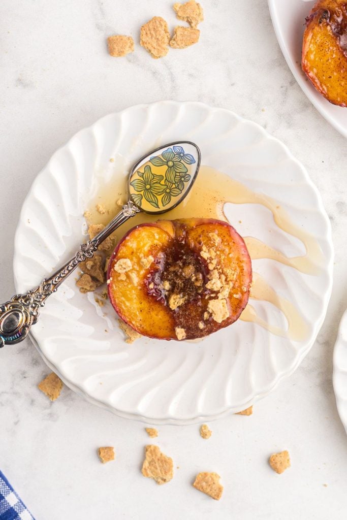 Juicy peach on a white plate with a silver and blue spoon drizzling honey on top 