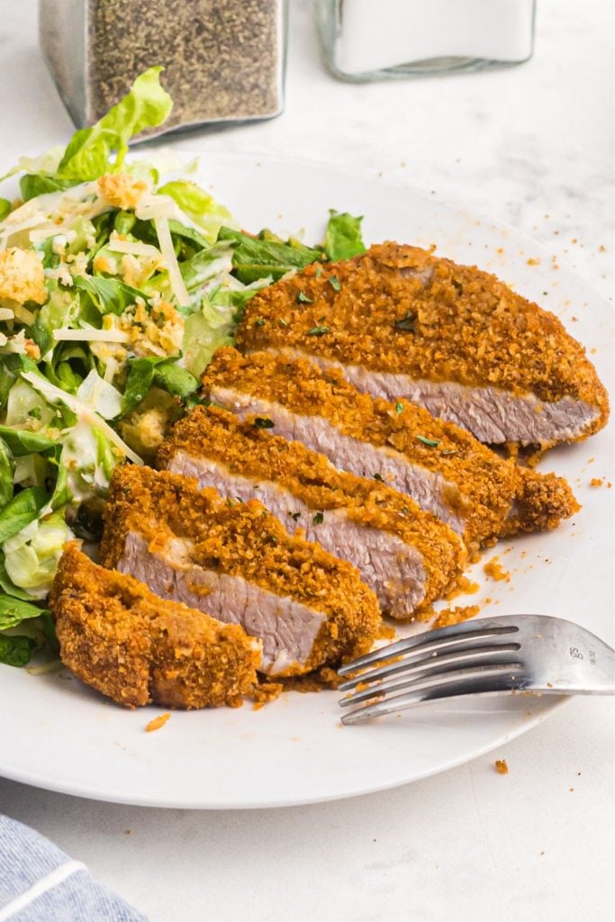 Golden crispy pork chops sliced and served on a white plate with salad