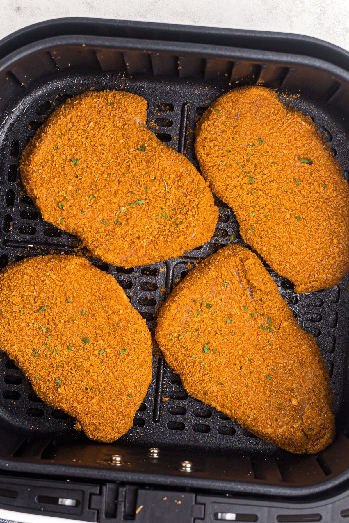 Uncooked coated pork chops in the air fryer basket