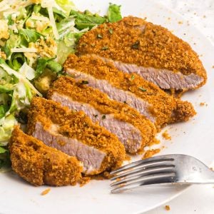 Golden crispy pork chop sliced on a white plate with salad and a fork