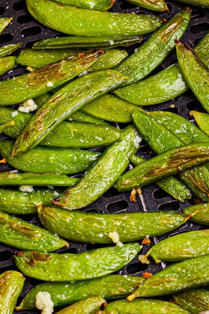 Green juicy snap peas in the air fryer basket tossed with garlic and sesame oil.