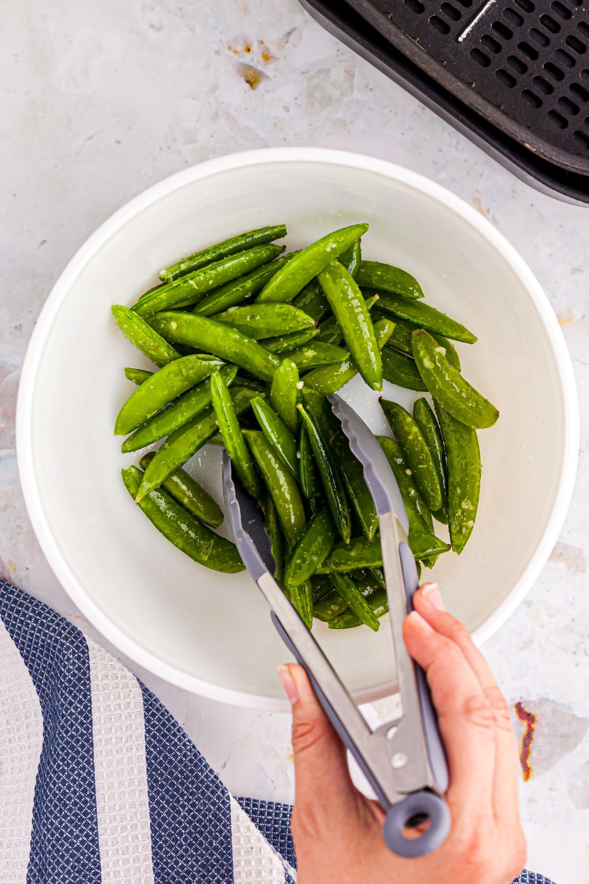 White bowl with snap peas being tossed in sesame oil and seasonings.