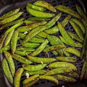 Juicy green snap peas in the air fryer basket after being cooked in the air fryer