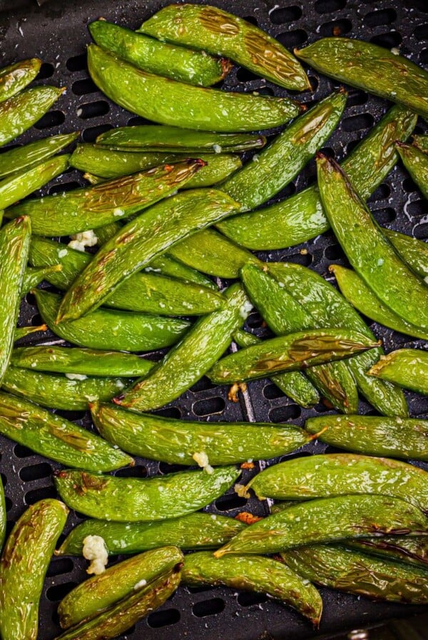 Juicy green snap peas in the air fryer basket after being cooked in the air fryer