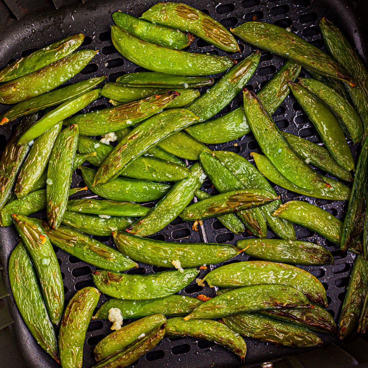 Juicy green snap peas in the air fryer basket after being cooked in the air fryer
