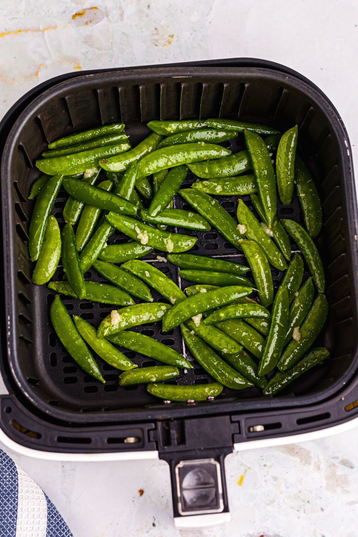 Green Snap peas tossed with olive oil in the air fryer basket before being cooked
