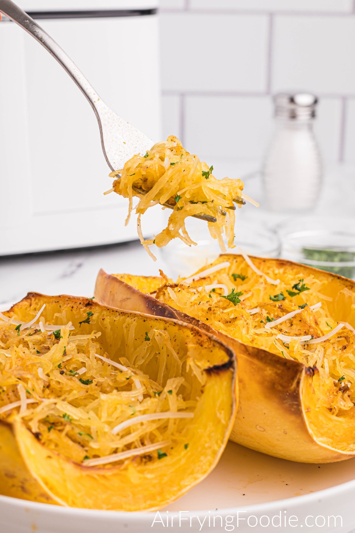 Spaghetti Squash made in the air fryer and topped with fresh parsley and parmesan cheese, with a bite on a fork. 