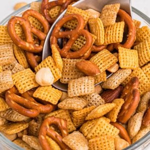 Clear bowl filled with chex mix on a white table with spoon scooping some out