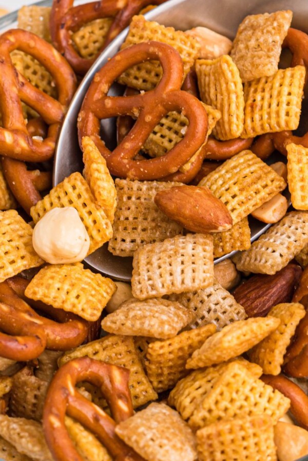 Clear bowl filled with chex mix on a white table with spoon scooping some out