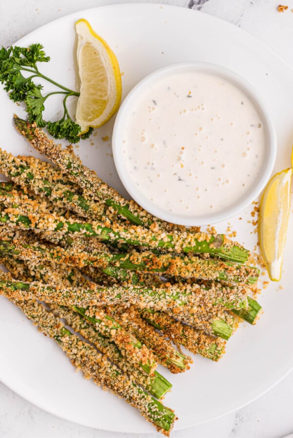 Plated air fried asparagus fries with lemon wedges and dipping sauce.