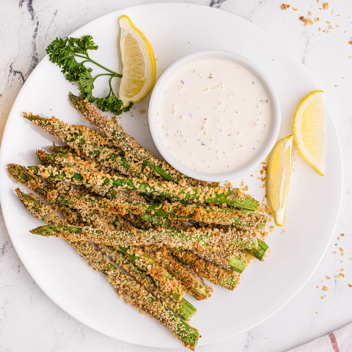 Plated air fried asparagus fries with lemon wedges and dipping sauce.