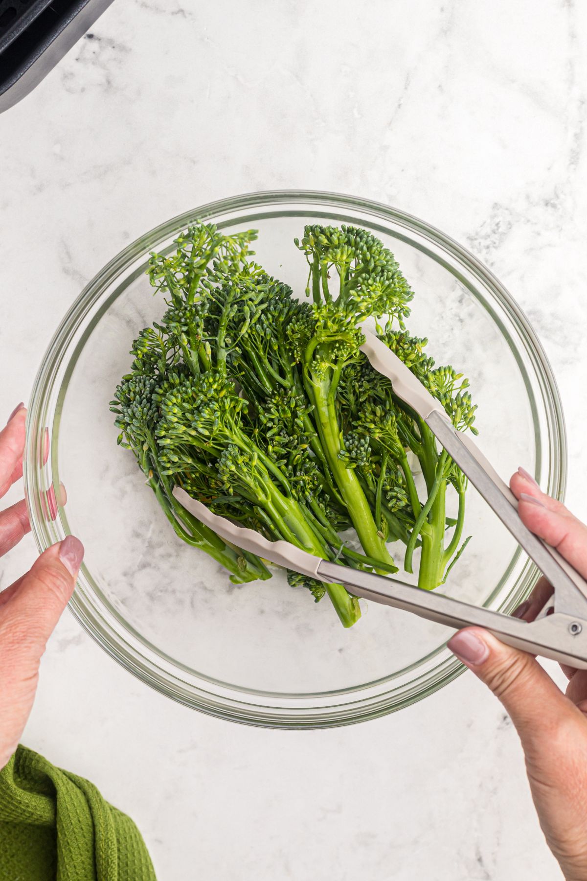 Broccolini florets being tossed in a glass bowl with garlic and seasonings