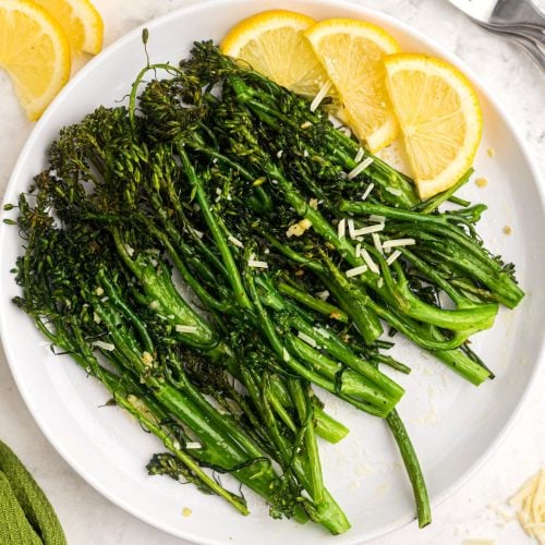 Juicy green broccolini florets on a white plate with lemon wedges