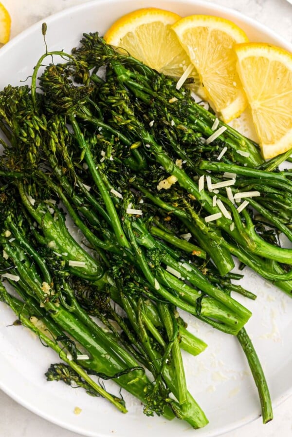 Juicy green broccolini florets on a white plate with lemon wedges