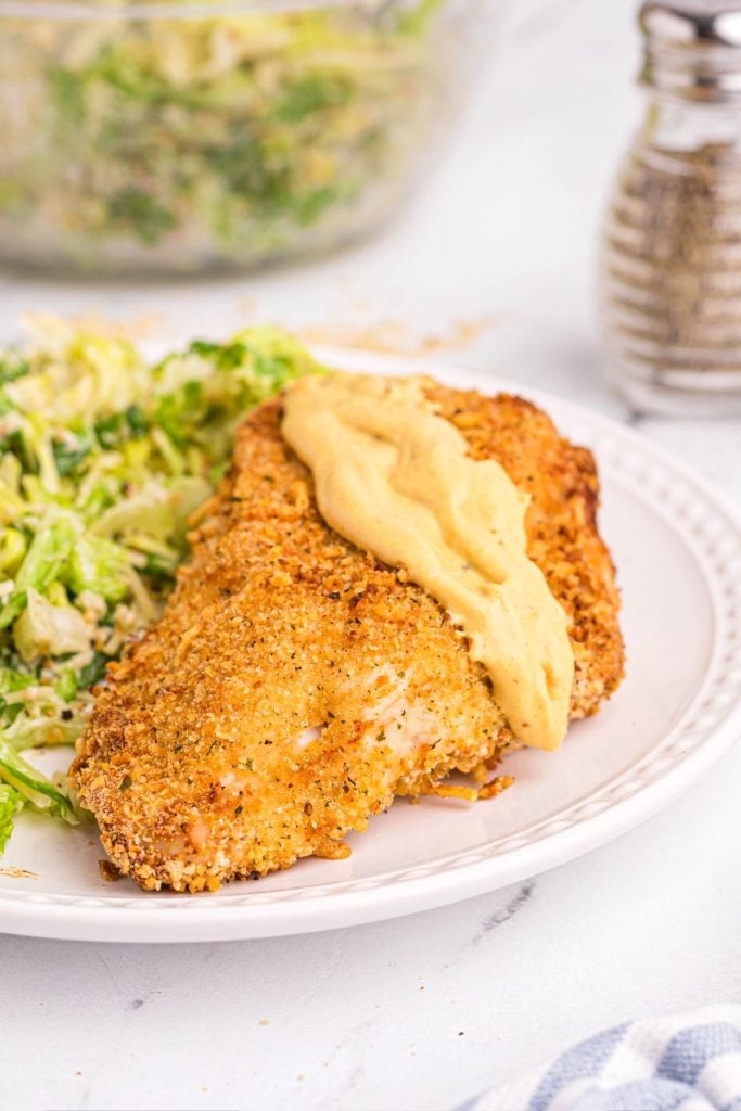 golden crispy chicken served with Dijon mustard and salad on a white plate