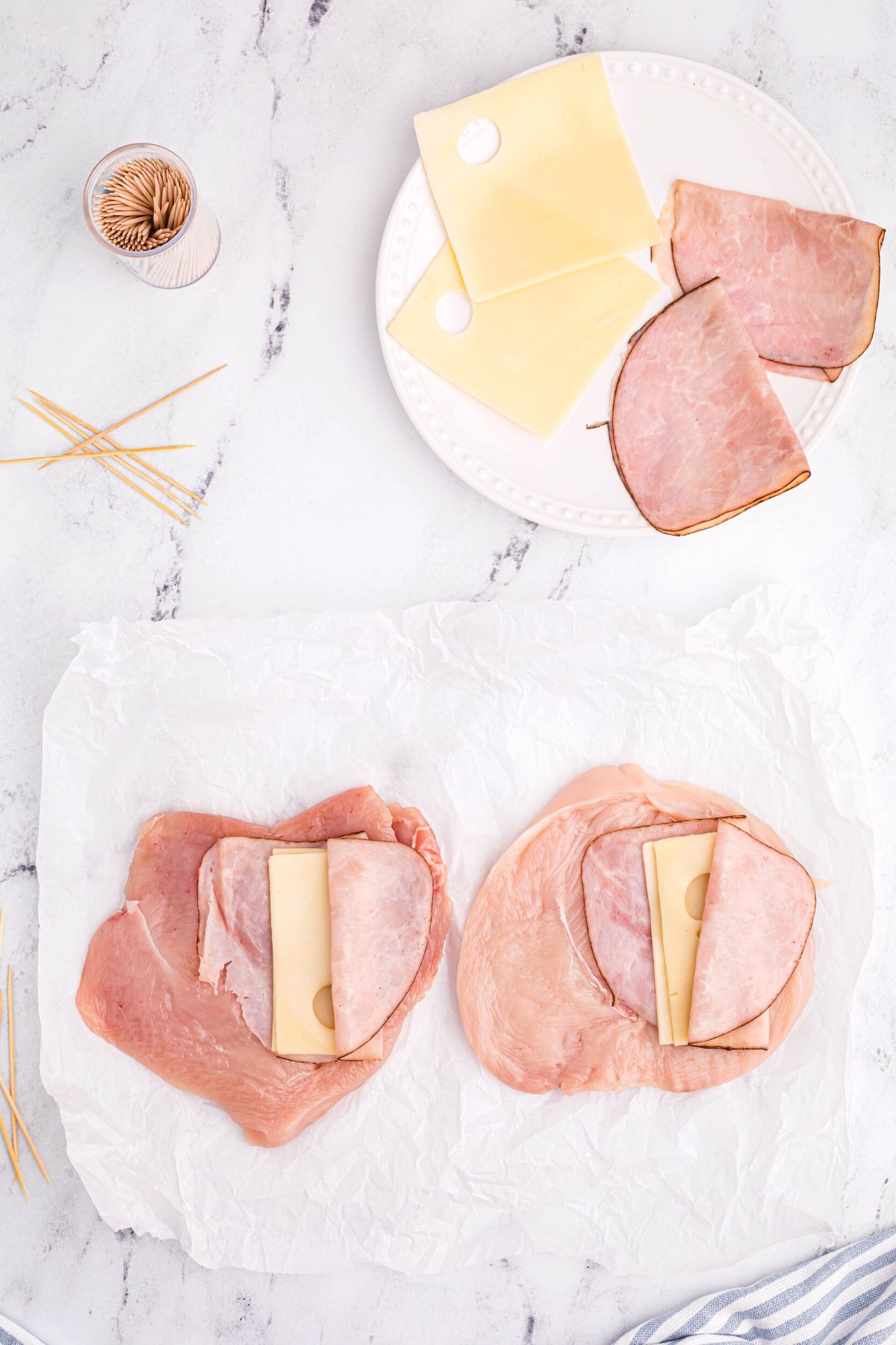 Uncooked chicken breasts sliced open and flattened, then filled with ham and cheese slices
