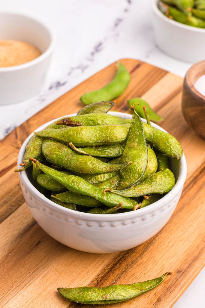 Green edamame pods in a white bowl after being cooked in the air fryer basket