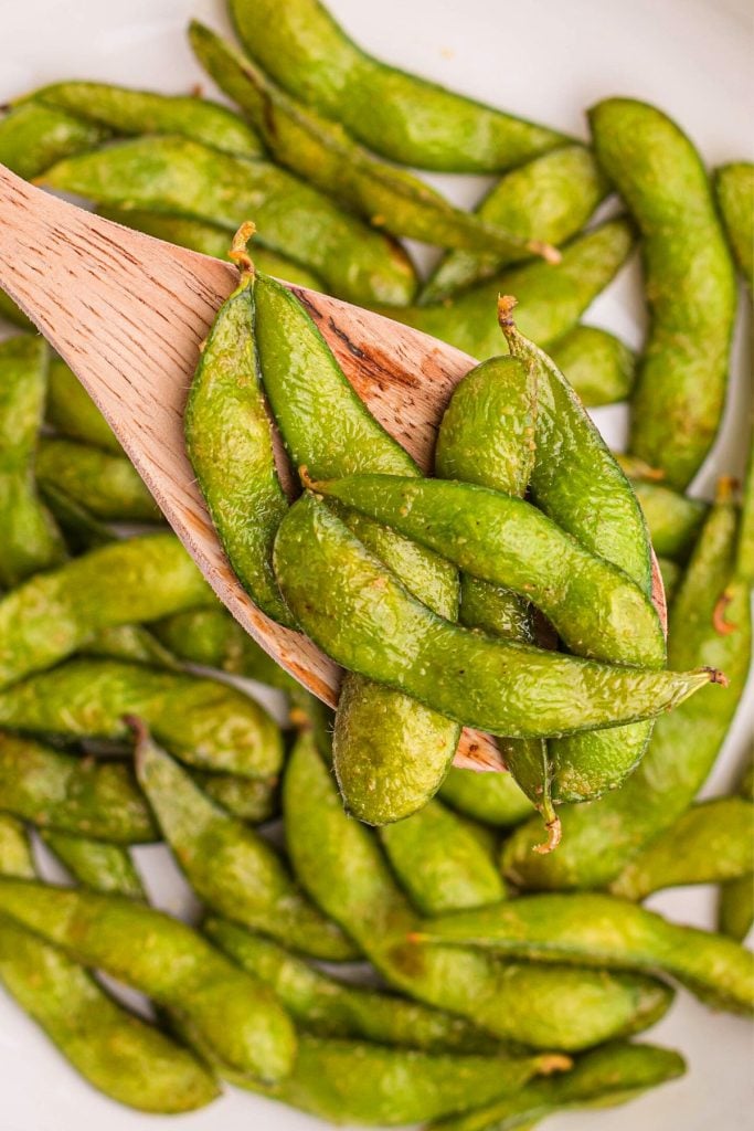 Bright green edamame pods seasoned and being scooped with a wooden spoon