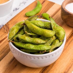 Bright green edamame pods in a white bowl served on a wooden cutting board