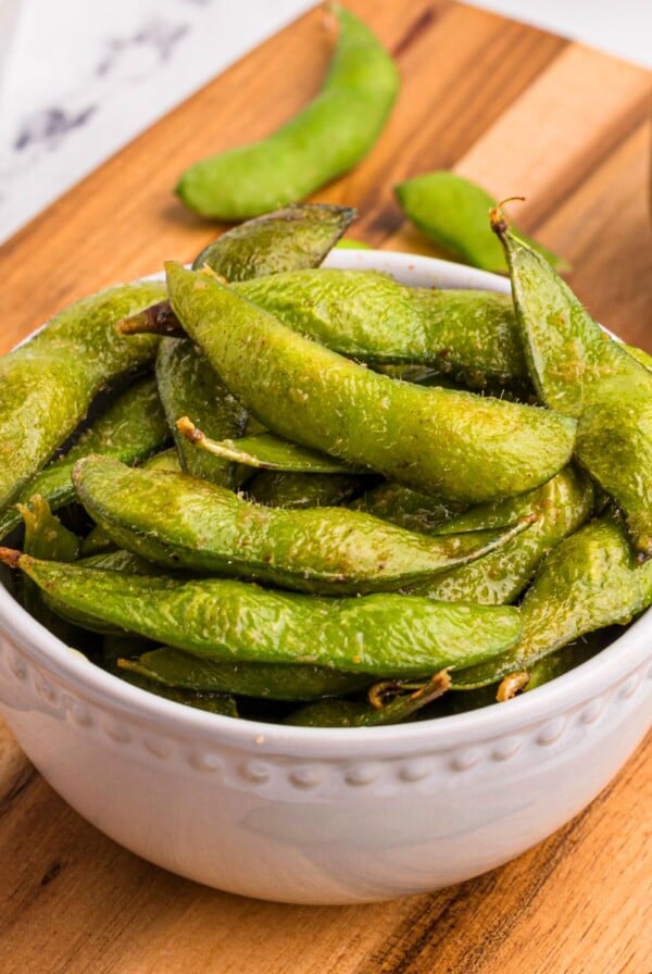 Bright green edamame pods in a white bowl served on a wooden cutting board