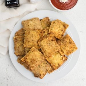 Overhead shot of fried ravioli made in the air fryer and served on a white plate.