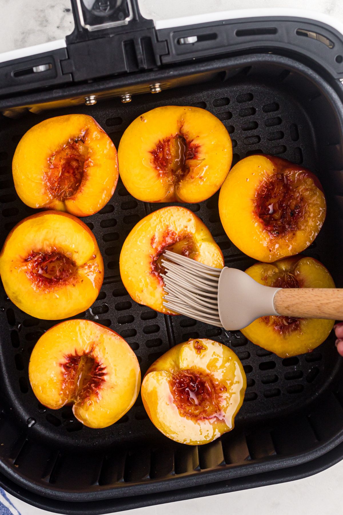 Golden yellow peaches being brushed with coconut oil in the air fryer basket