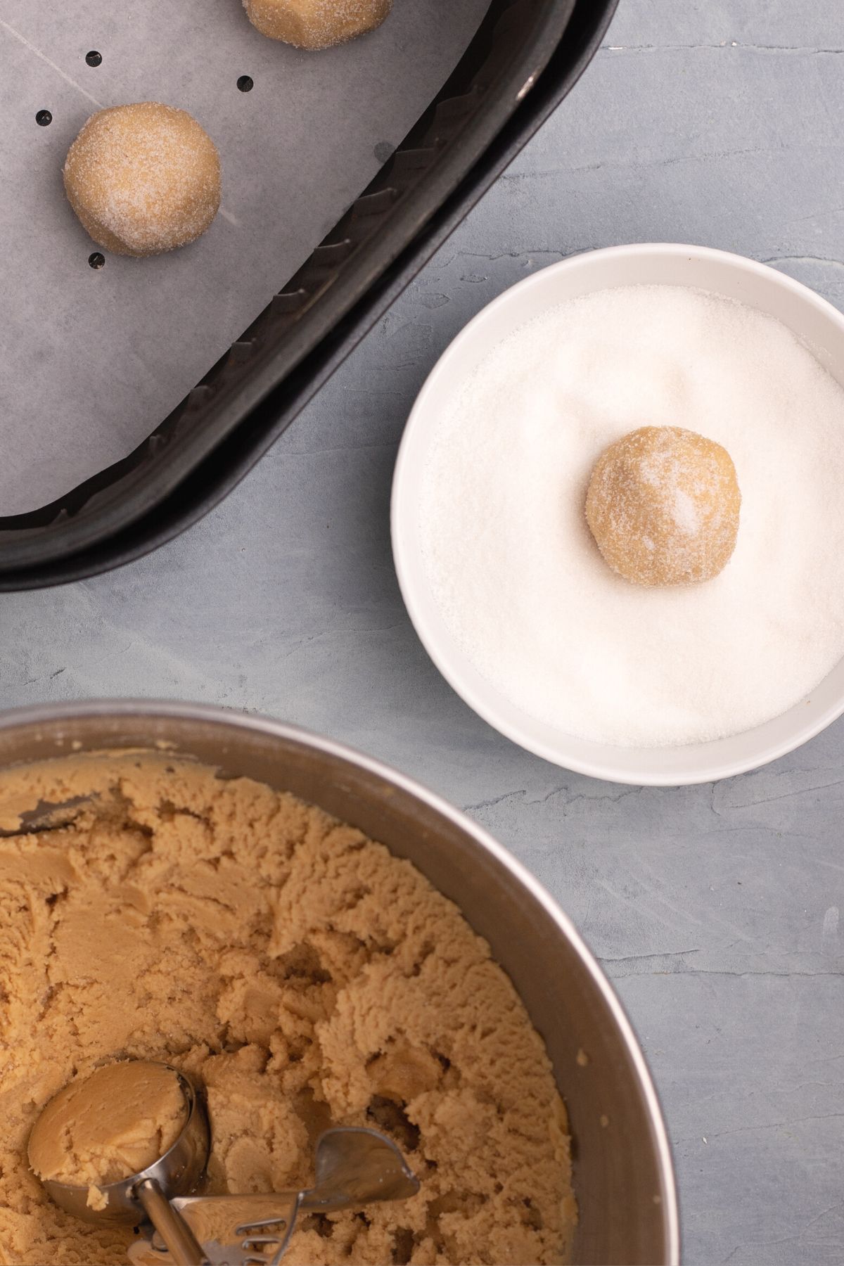 Scoops of dough being coated with sugar and then placed in the air fryer basket lined with parchment paper