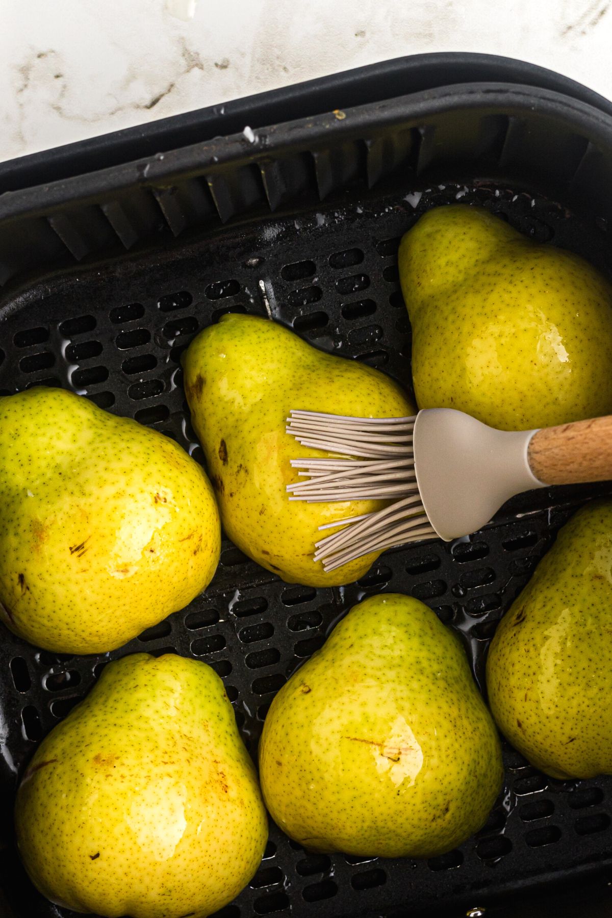 Brushing coconut oil on pear halves in the air fryer basket.