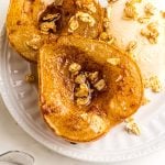 Close up of pear halved and coated with melted butter and cinnamon brown sugar, then topped with granola and served with ice cream on a white plate