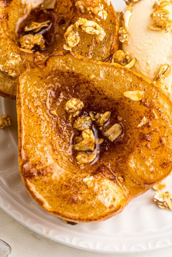 Close up of pear halved and coated with melted butter and cinnamon brown sugar, then topped with granola and served with ice cream on a white plate