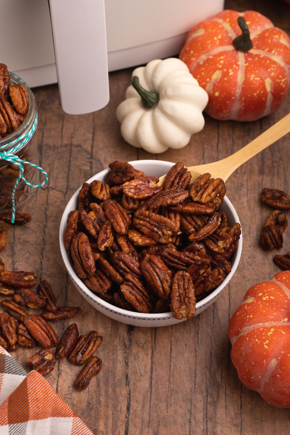Pumpkin spice pecans in a bowl with a wooden spoon scooping some out.