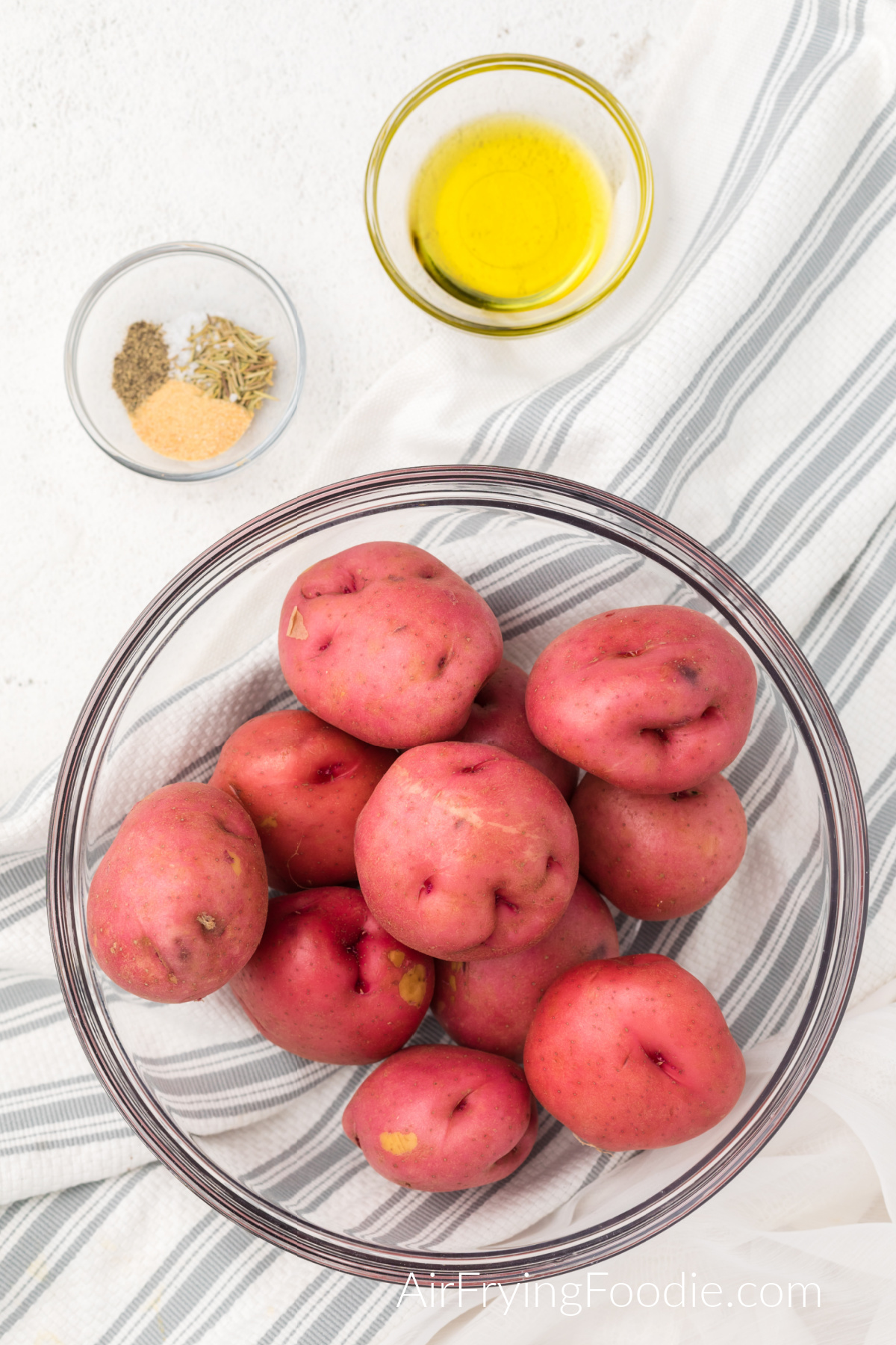 Ingredients for air fryer red potatoes. baby red potatoes in a dish, seasonings in a dish, and olive oil in a dish. 