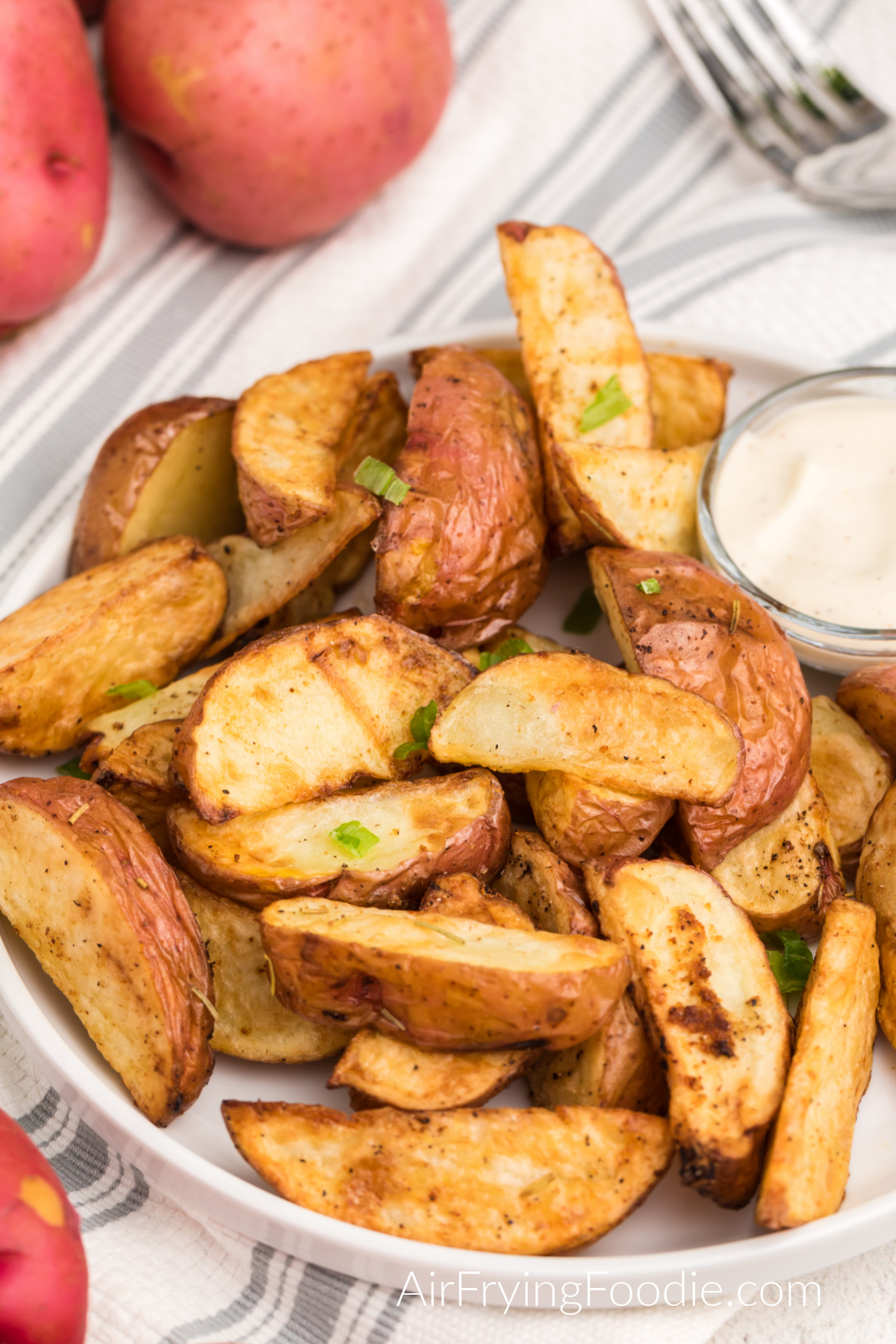 Seasoned air fried red potatoes on a plate with dipping sauce. 