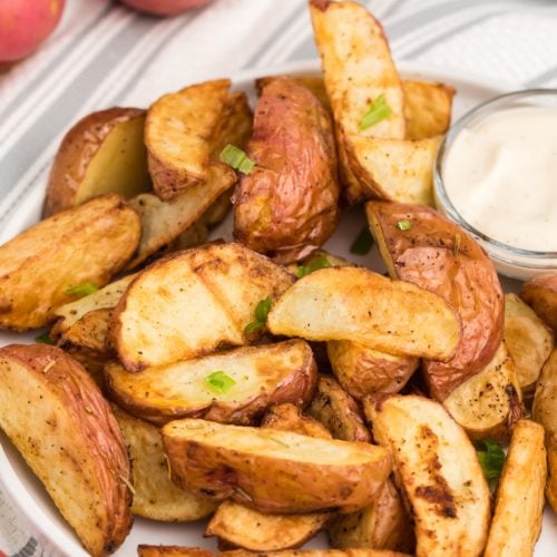 Seasoned air fried red potatoes on a white plate with dipping sauce, ready to eat.
