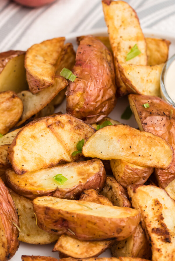 Seasoned air fried red potatoes on a white plate with dipping sauce, ready to eat.