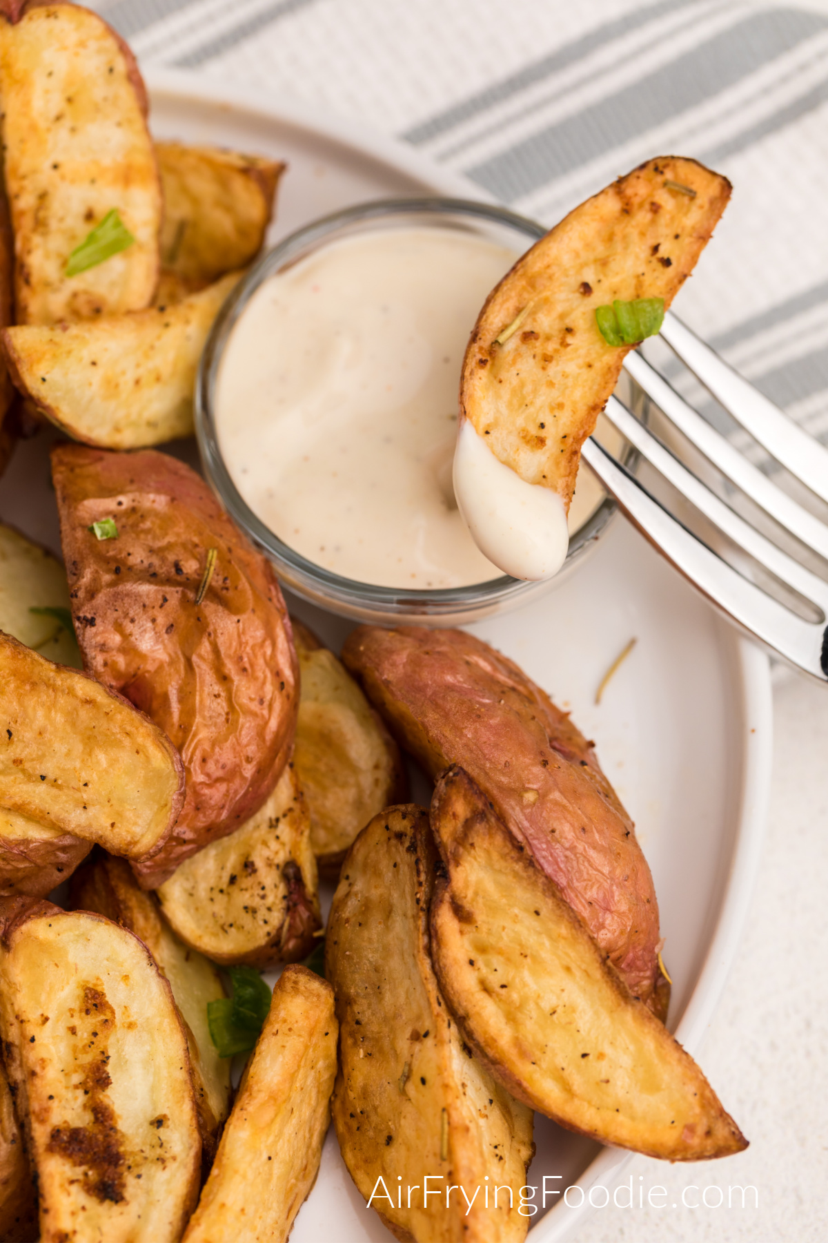 Air Fried Red Potatoes seasoned and on a white plate with dipping sauce, with one on a fork ready to eat.