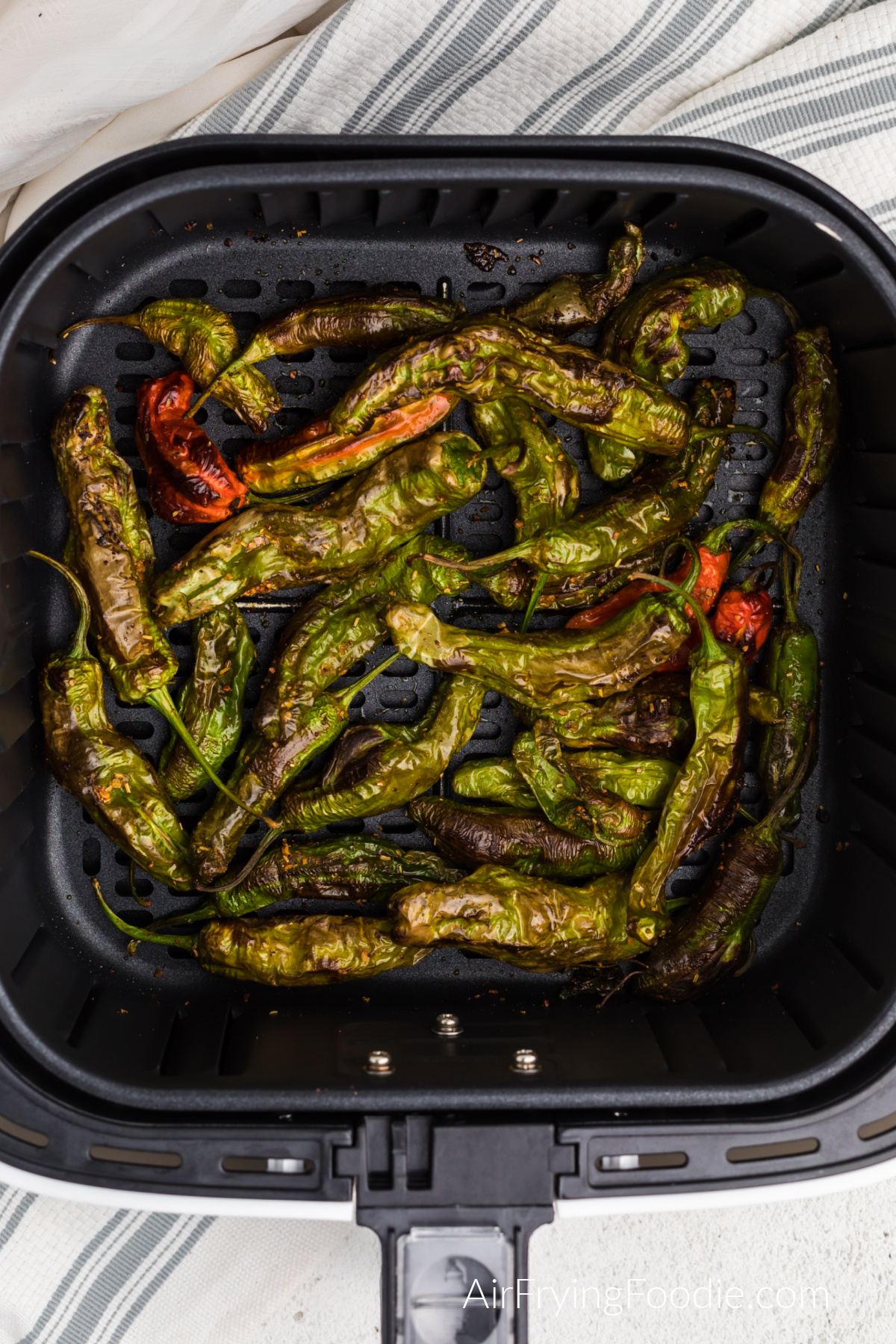 Air fried shishito peppers in the basket of the air fryer.