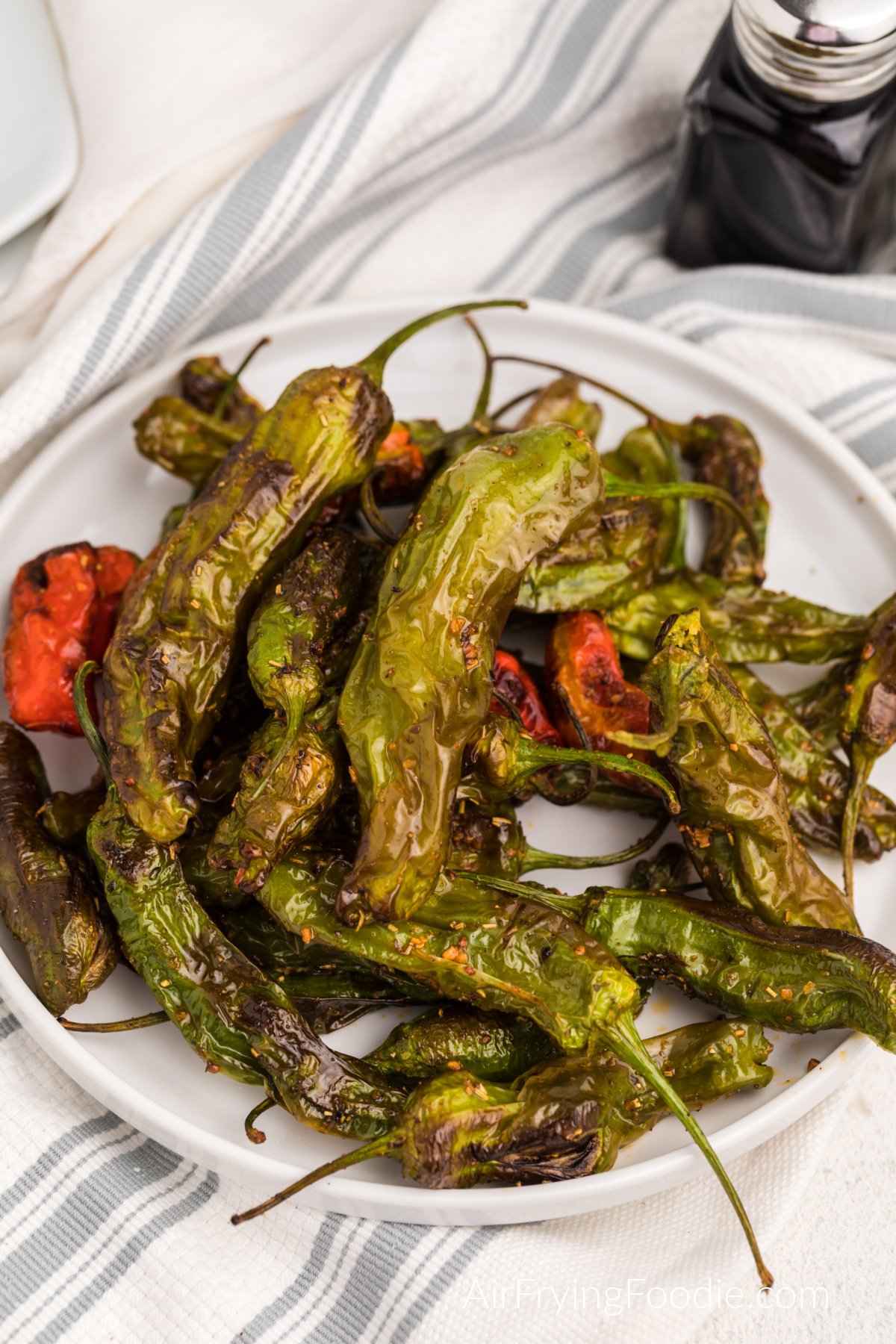 Air fried shishito peppers on a white plate ready to serve.