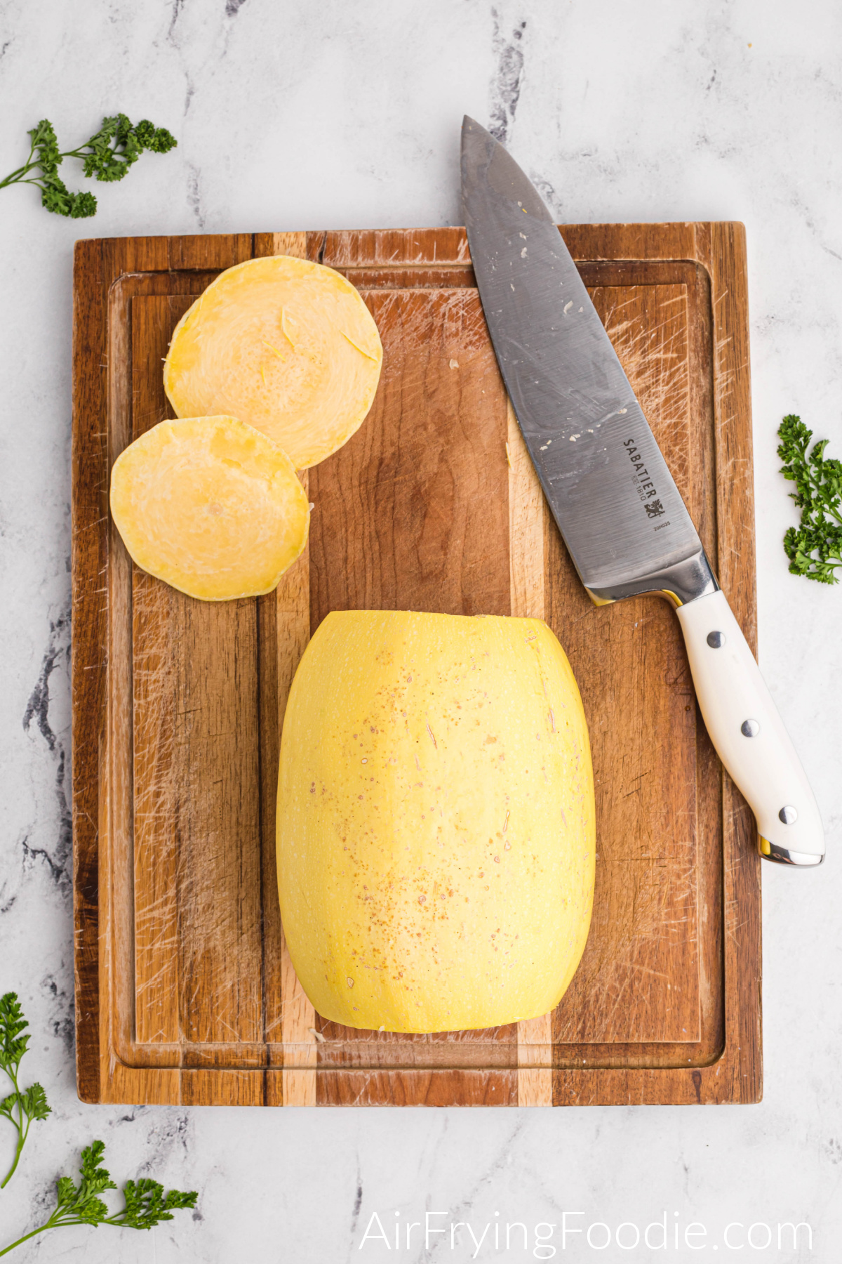 Spaghetti squash with ends cut, on a cutting board with a knife.