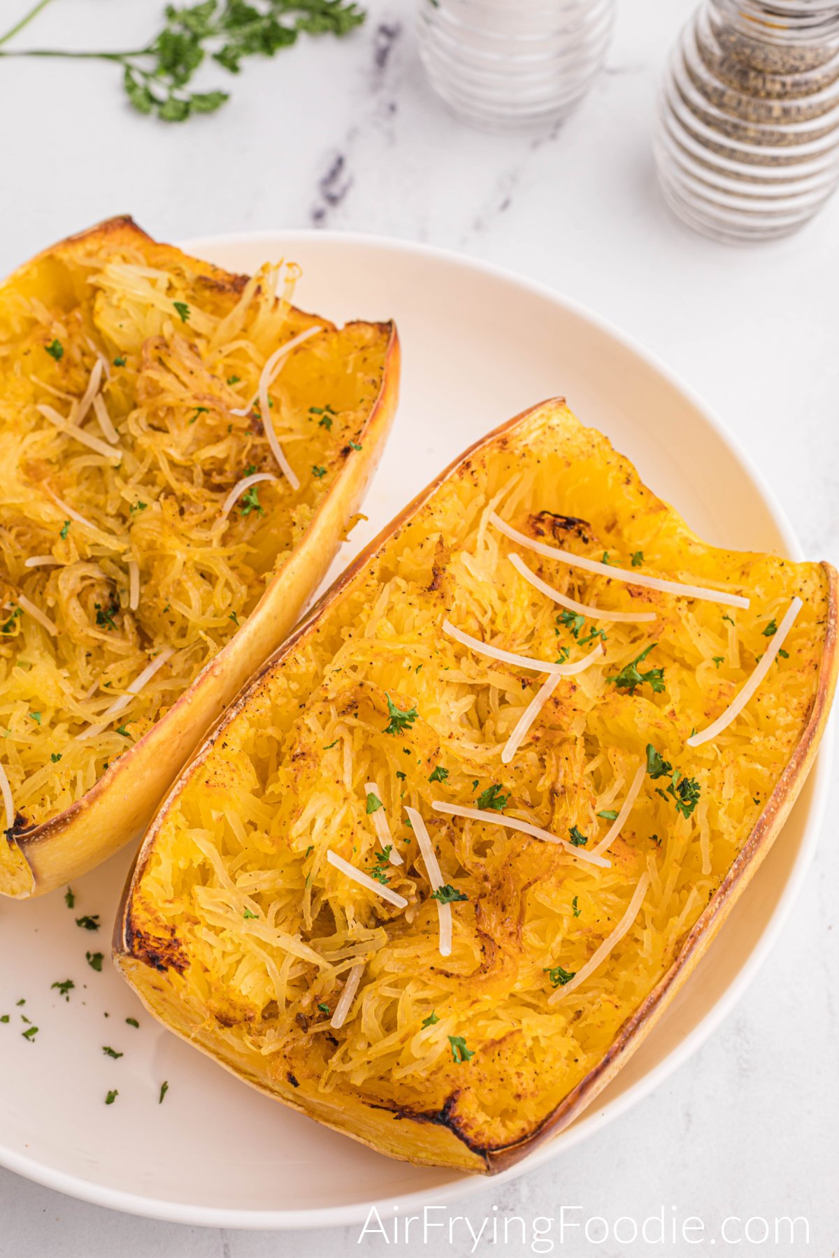 Spaghetti squash on a white plate that's been fluffed and topped with shredded parmesan and fresh parsley.